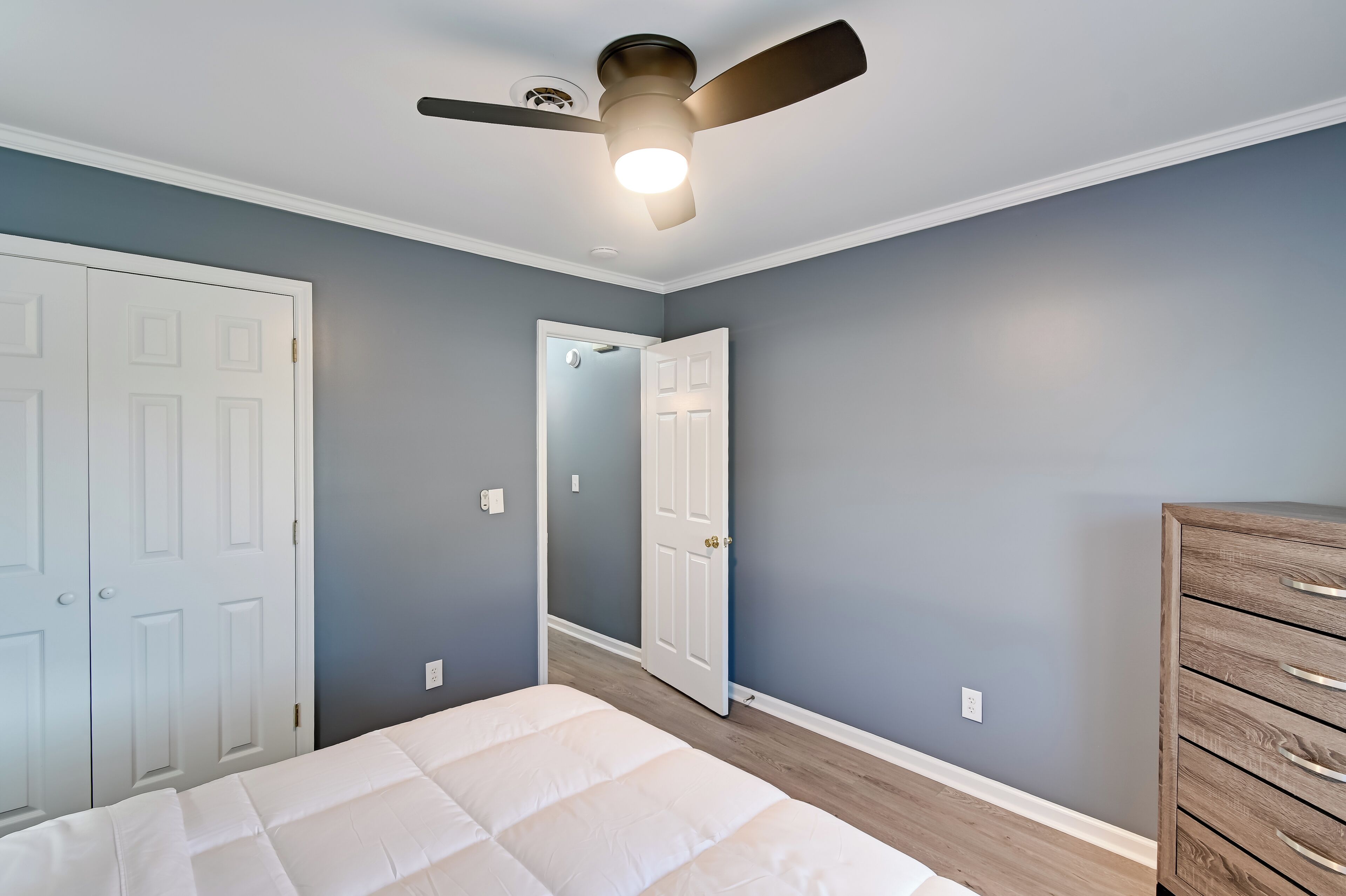 A bedroom with a bed, a ceiling fan, a dresser, and a door.