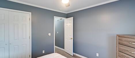 A bedroom with a bed, a ceiling fan, a dresser, and a door.