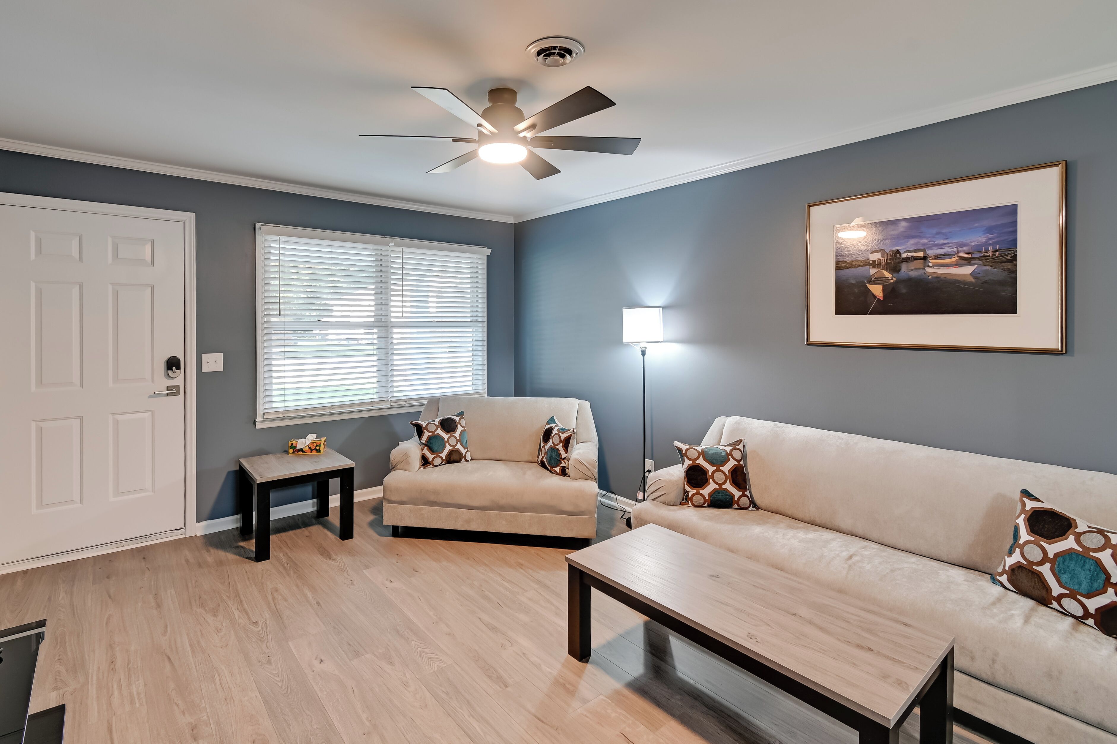 A living room with a beige sofa, a coffee table, a floor lamp, and a ceiling fan.