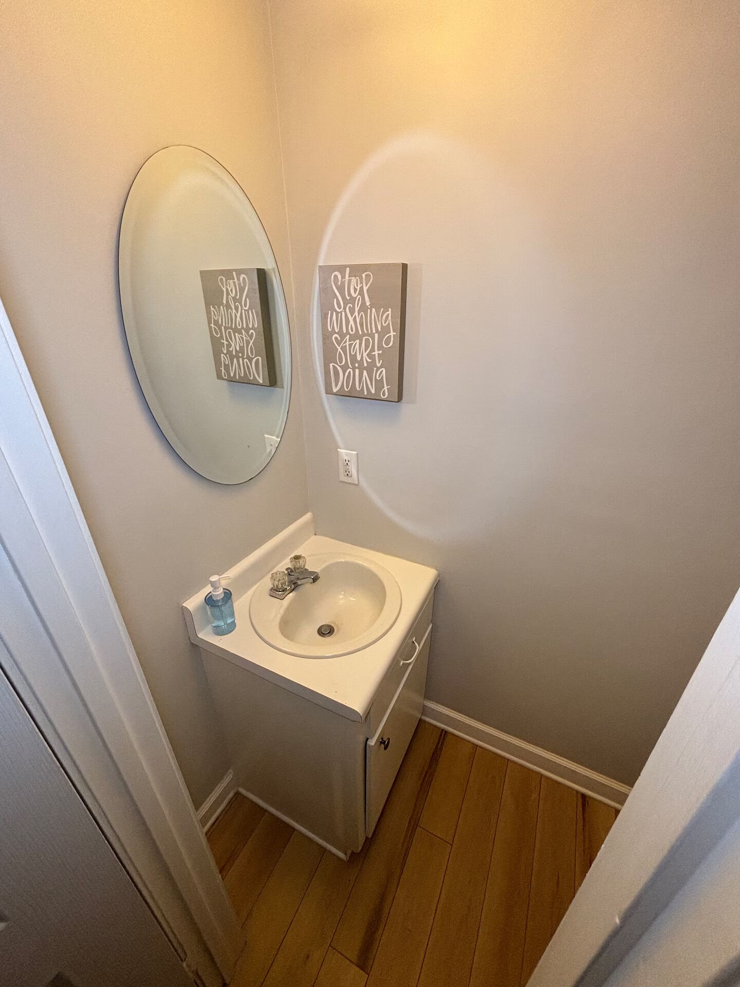 A bathroom with a round mirror, a sink, and a motivational quote on the wall.