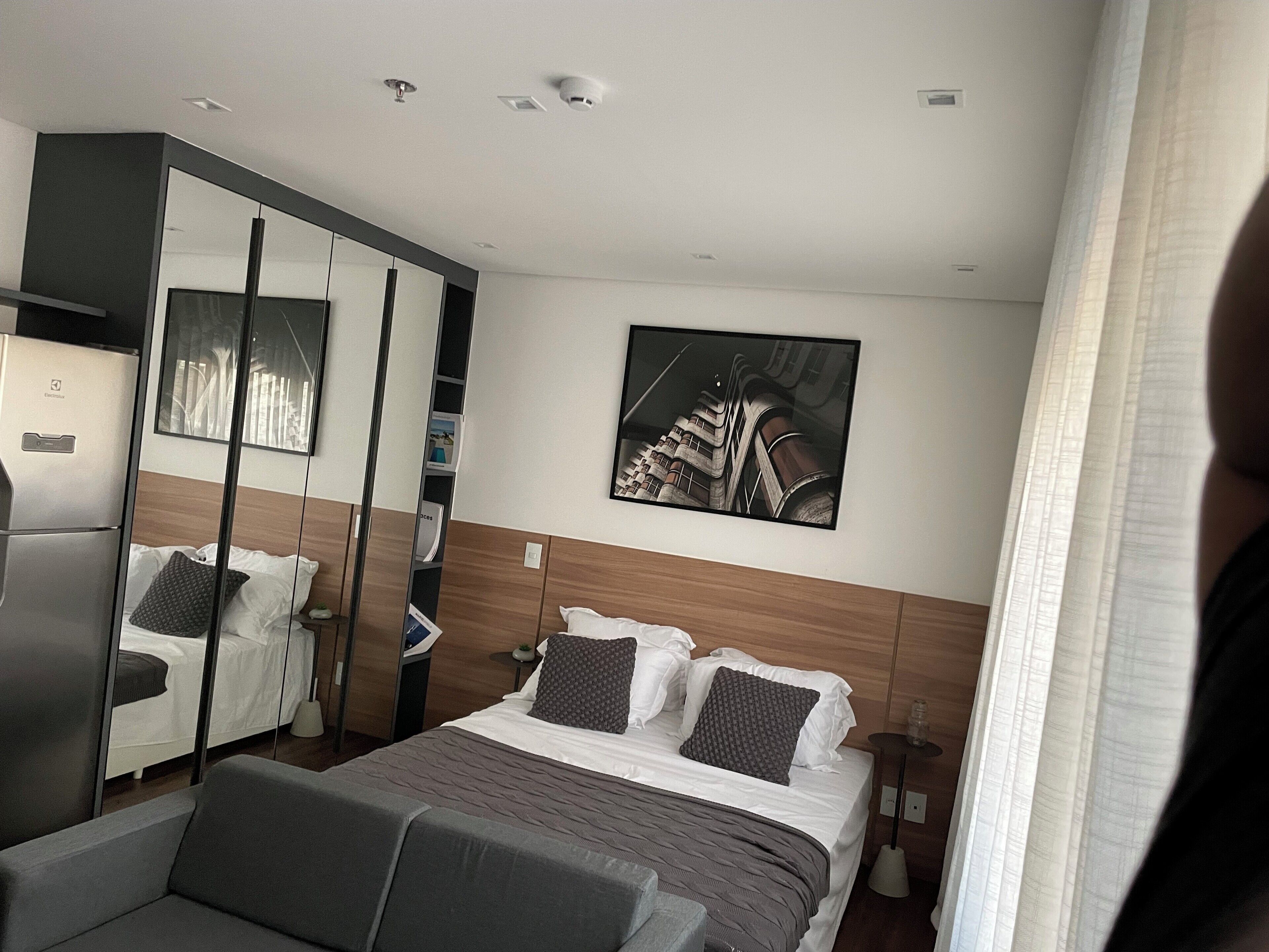 A modern hotel room with a bed, a sofa, a wardrobe, and a painting on the wall.
