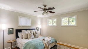 A bedroom with a bed, a ceiling fan, two windows, a bedside table, and a floor lamp. - < 1 Mi to Ole Miss & The Grove! Charming Getaway (Oxford)
