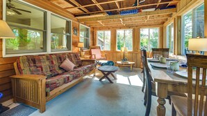 A cozy cabin interior with a wooden ceiling, large windows, a sofa, a dining table, and chairs. - Waterfront Escape w/ Beach Access in Bridgton (Bridgton)