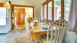 A dining area with a wooden table and chairs, a refrigerator, and a window with curtains. - Waterfront Escape w/ Beach Access in Bridgton (Bridgton)