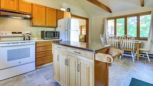 A kitchen with wooden cabinets, a refrigerator, a microwave, and a stove. There is a dining area with a table and chairs. - Waterfront Escape w/ Beach Access in Bridgton (Bridgton)