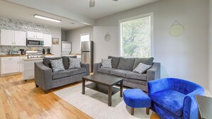 A modern living room with two grey sofas, a coffee table, and a blue armchair. A ceiling fan and a large window with blinds are visible. - 9 Mi to Dtwn ATL: Pet-Friendly Apt w/ Yard (Atlanta)
