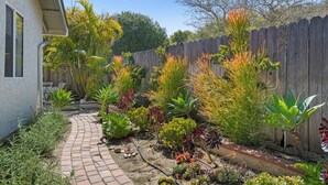 Un jardin avec un chemin en briques, différentes plantes et une clôture en bois.