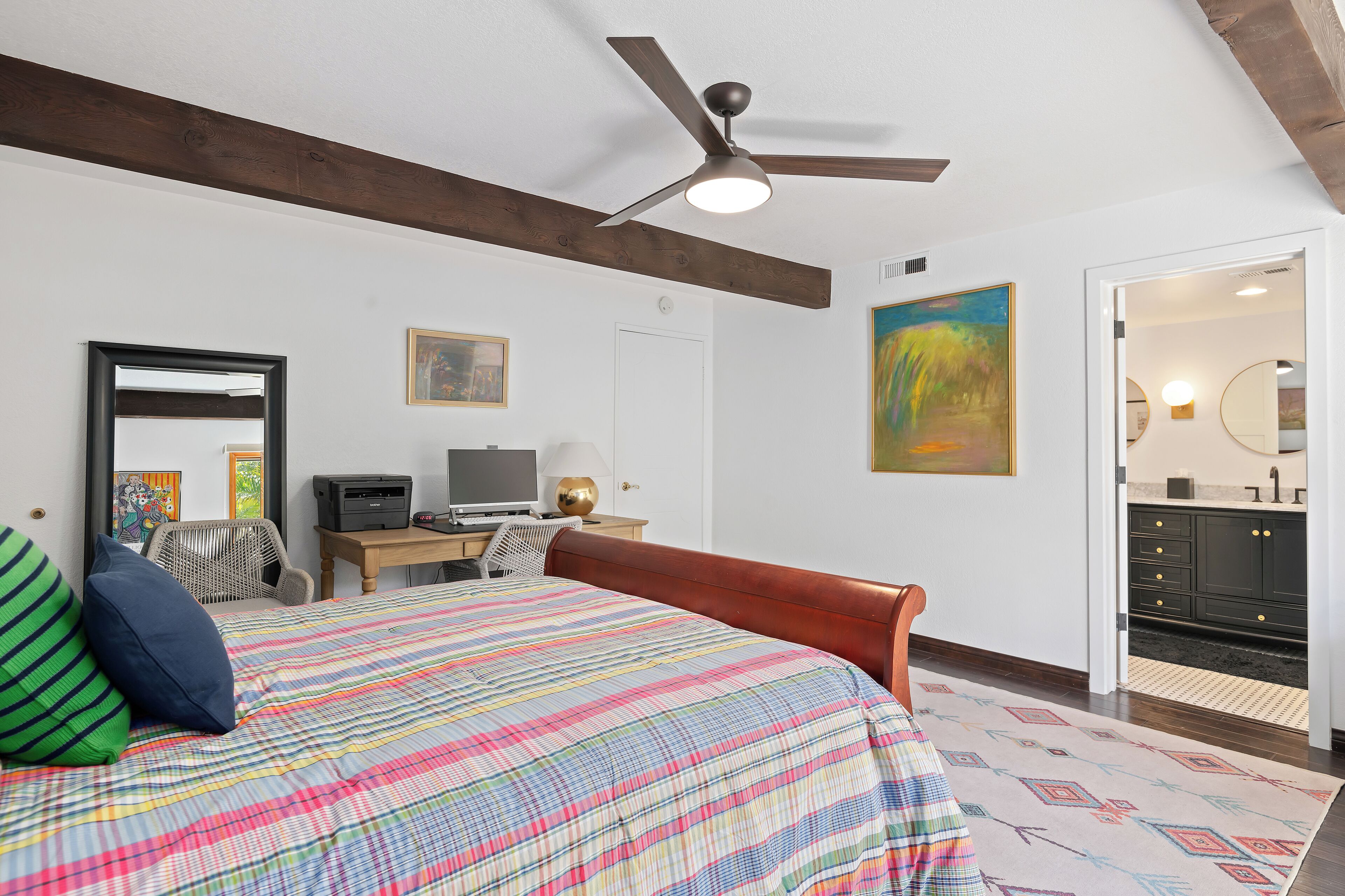 A bedroom with a bed, a desk, a chair, a ceiling fan, and a bathroom visible through an open door.