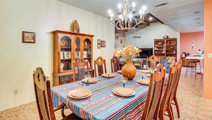 Un comedor con una mesa dispuesta para cuatro personas, rodeada de sillas de madera. Un candelabro cuelga del techo, y se aprecia un aparador de madera con puertas de cristal en el fondo.