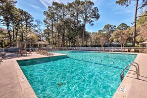 Uma piscina azul cristalina com um deck de madeira, espreguiçadeiras e um gazebo.