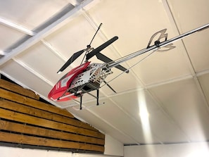 Un helicóptero rojo con fuselaje metálico y hélice, suspendido del techo en una habitación con paredes blancas y vigas de madera.