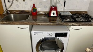 Eine kompakte Küche mit integrierter Waschmaschine und Trockner, einem Edelstahlspülbecken, einem roten Mixer und einem Gasherd.