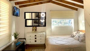 Ein Schlafzimmer mit schrägverdeckter Decke, einem Bett, einer Kommode, einem Spiegel und einem Fenster.