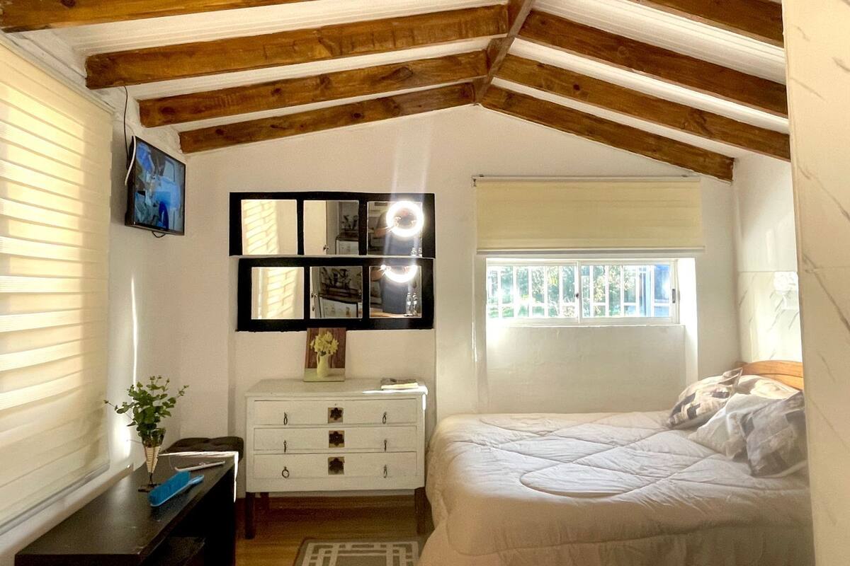 A bedroom with a sloped ceiling, a bed, a dresser, a mirror, and a window.