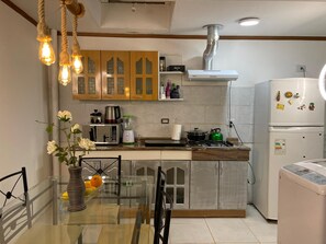 Una cocina moderna con zona de comedor, que incluye una mesa de vidrio, sillas, un florero con flores y diversos electrodomésticos.