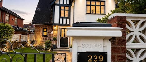 A two-story house with a black and white exterior, a well-maintained garden, and a gate labeled 'SCUTARI 239 SEYMOUR GROVE'.