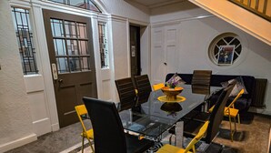 Un coin repas avec une table en verre, des chaises noires et jaunes, un canapé et une petite fenêtre ornée d’un tableau.
