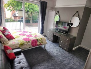 Een slaapkamer met een bed, een dressoir, een televisie en een raam met gordijnen.