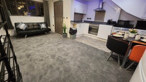 A modern kitchen with a built-in oven, microwave, and a stainless steel range hood. There is a dining table with chairs and a small potted plant. - Annexe Ground Apartment Charming Tudor style Apartment (Stretford)