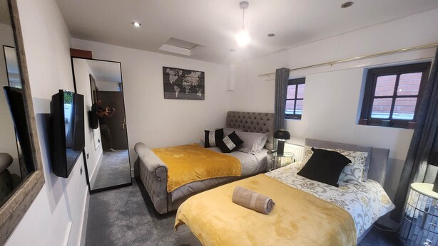 A hotel room with two beds, a large mirror, a world map on the wall, and a window with curtains. - Annexe Ground Apartment Charming Tudor style Apartment (Stretford)