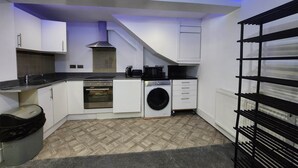 A compact kitchen with white cabinets, a built-in oven, a washing machine, and a black countertop. - Annexe Ground Apartment Charming Tudor style Apartment (Stretford)