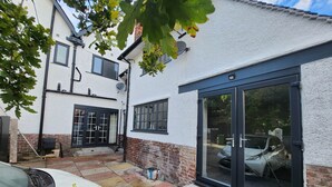 A white building with a garage, a car parked in front, and a tree with green leaves. - Annexe Ground Apartment Charming Tudor style Apartment (Stretford)