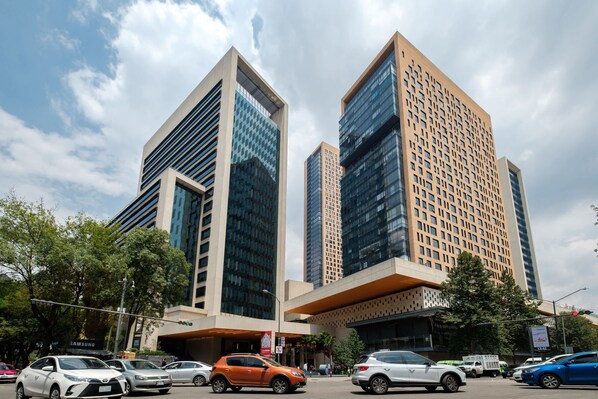 A modern building with a glass facade and a flat roof, surrounded by parked cars and trees.
