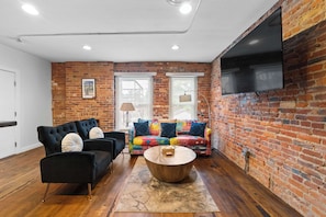 A living room with a black sofa, colorful sofa, and a wooden coffee table. - Short North Loft Free Parking Sleeps 2 (Columbus)