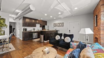 Sala de estar moderna com sofá, mesa de centro e cozinha ao fundo.