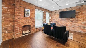 Ein Zimmer mit Backsteinwand, Kamin, Wand-Fernseher und einer schwarzen Couch.