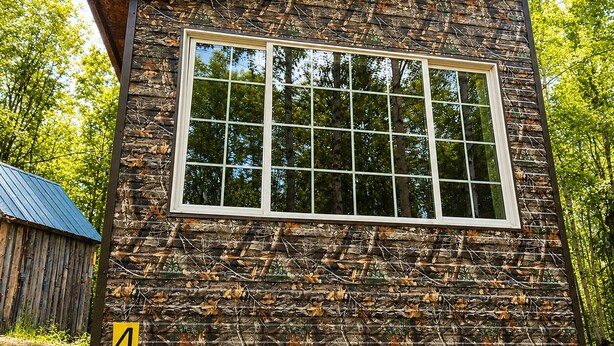A cabin with a large window, wooden structure, and a number 4 sign. - Camo Cabin #4 (Houston)