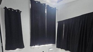 A bedroom with a bed, a ceiling fan, and two windows with black curtains. - Camo Cabin #4 (Houston)