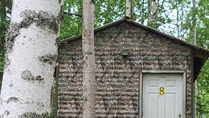 En liten stuga av trä med en vit dörr som har nummer 8 målat på sig, omgiven av träd.