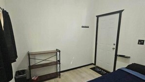 A small, sparsely furnished room with a bed, a door, a ceiling fan, and a window. - Camo Getaway Cabin #7 (Houston)