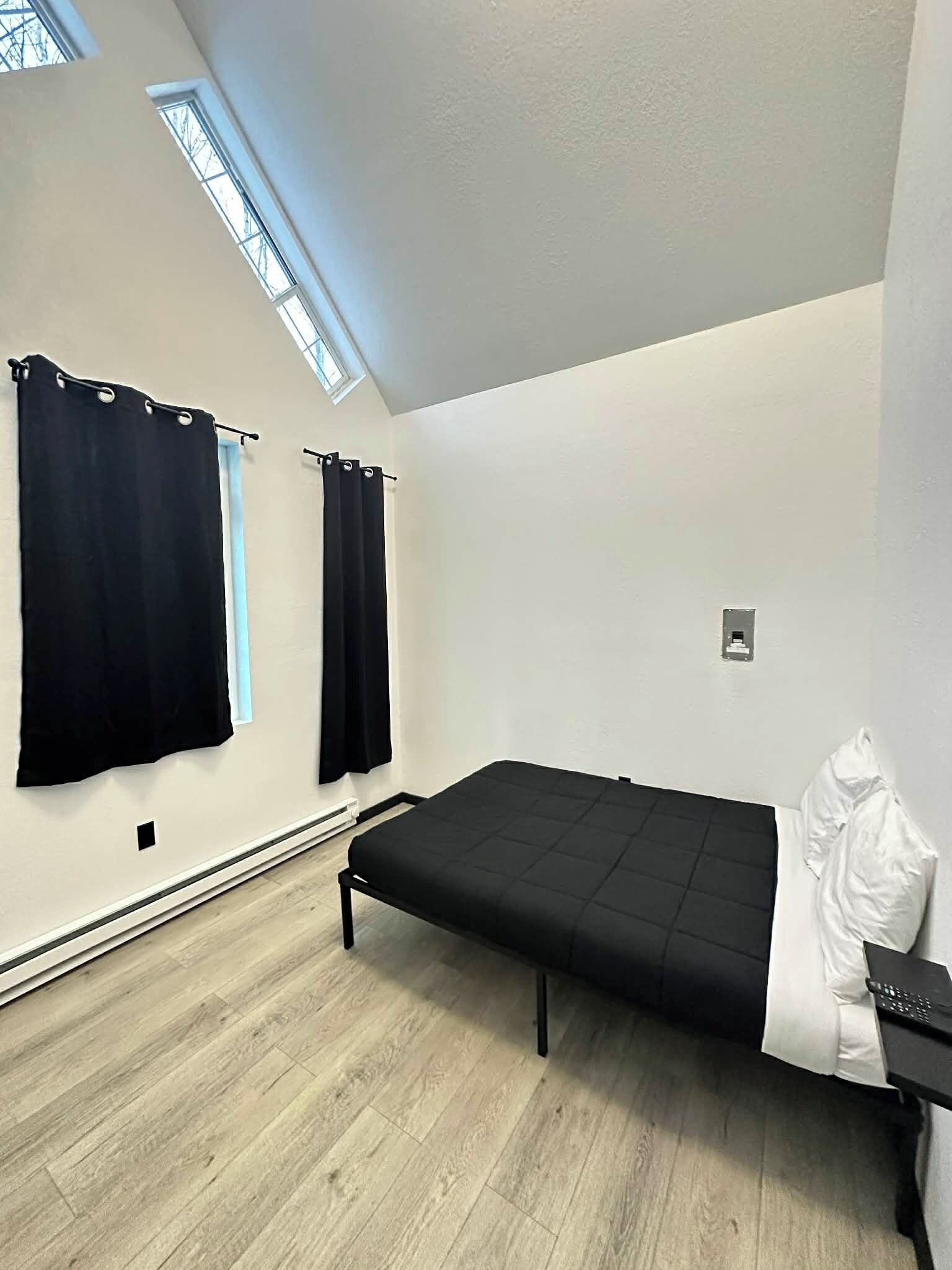 Una habitación moderna y minimalista con una cama, una mesita y una ventana con cortinas.