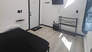 A minimalist bedroom with a bed, a door, a TV mounted on the wall, and a small window. - Rustic Bunk #5 (Houston)