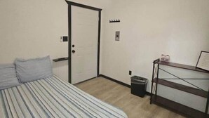 A bedroom with a bed, a ceiling fan, a door, a small trash bin, and a desk with a chair. - Mat-Su Thunder Cabin #1 (Houston)