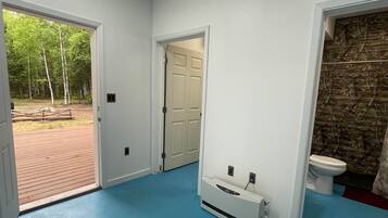 A room with a blue floor, a white door, a white radiator, and a view of a wooden deck and trees.