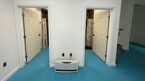 A hallway with two doors leading to bathrooms, a white heater in the center, and a blue carpet. - Vibing In The Woods #6 (Houston)