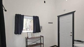 A bedroom with a bed, a window with curtains, a door, a ceiling fan, and a small shelf. - Vibing In The Woods #6 (Houston)