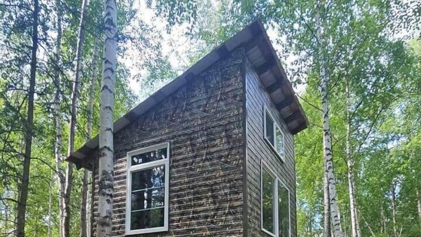 Uma cabana rústica com fachada de madeira, construída sobre pilares, cercada por uma floresta.