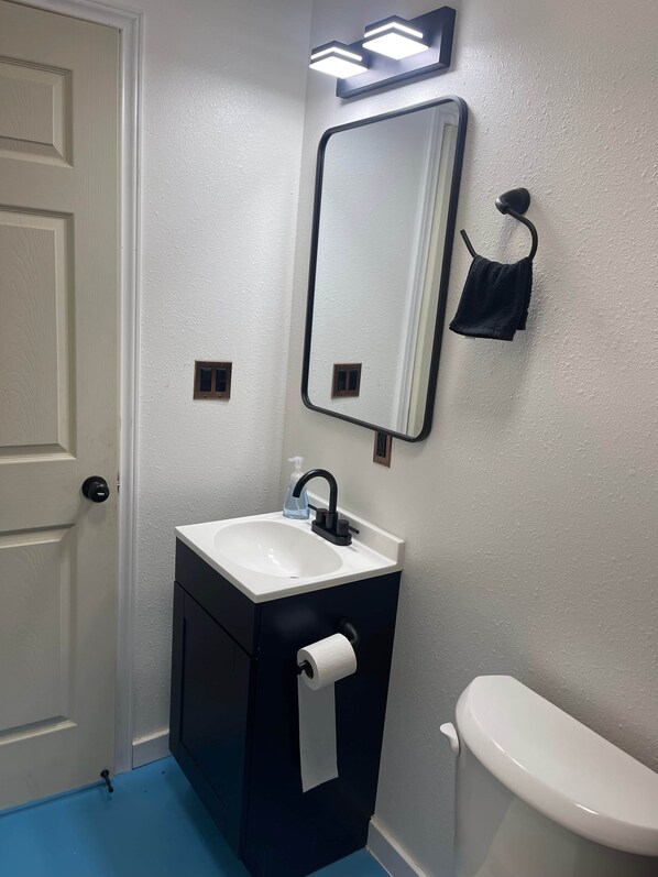Un baño con lavamanos blanco, mueble negro, inodoro, espejo y toallero.