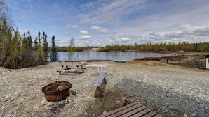 A lakeside picnic area with a fire pit, picnic tables, and a small cabin in the background. - Bass Farm: Lake View Loft Cabin (Houston)