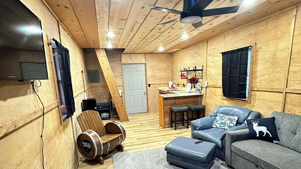 A cozy cabin interior with a wooden interior, a sofa, a dining table, and a ceiling fan. - Bass Farm: Lake View Loft Cabin (Houston)