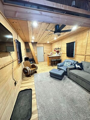 Interior acogedor de una cabaña con paredes y detalles de madera, un sofá, una mesa de comedor y un ventilador de techo.
