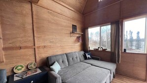 A cozy cabin room with a sofa bed, a small table with decorative plates, and a window with curtains. - Bass Farm: Lake View Loft Cabin (Houston)