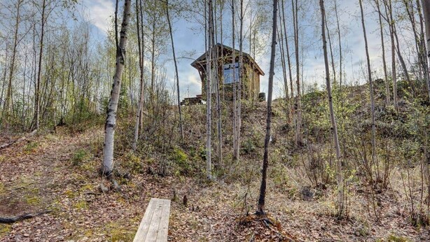 En træhytte omgivet af skov med en træterrasse i forgrunden.
