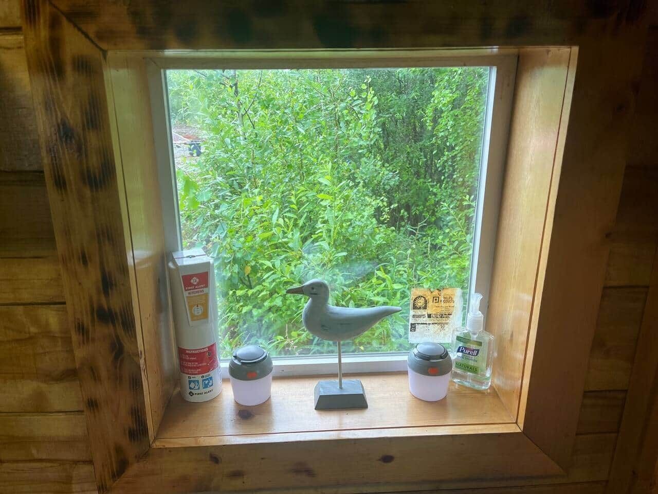 Un alféizar de madera con una figurita de pájaro, dos recipientes y una botella de desinfectante para manos.