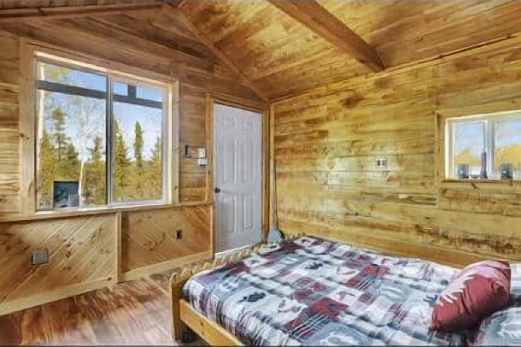 Camera in stile baita con soffitto in legno, un letto con biancheria a motivi decorativi, una finestra e una porta.