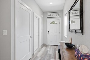 Un pasillo con puertas blancas, suelo de madera, un banco, un cuenco y un espejo en la pared.